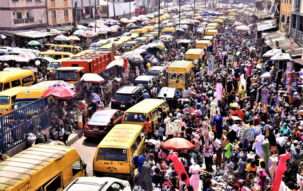 A busy Lagos street lined with market stalls and yellow danfo buses