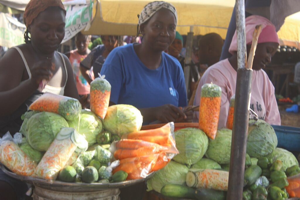 A Nigerian market trader smiling behind a stall of fresh produce